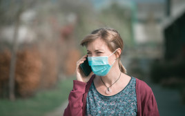 אישה עם מסכה מדברת בטלפון (צילום: אינג אימג')