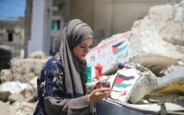 תושבת עזה מציירת דגל פלסטין על ביתה שנהרס במבצע "שומר חומות" (צילום: רויטרס)