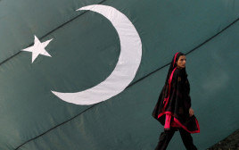 אישה עוברת ליד דגל פקיסטן (צילום: רויטרס)