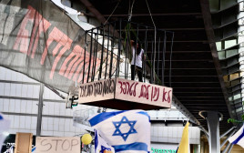 עינב צנגאוקר תלויה בכלוב מעל צומת בגין ביום השיבוש 7.7.24 (צילום: אבשלום ששוני)
