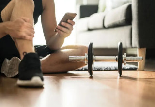 גבר עושה אימון כושר ביתי עם משקולות בעזרת הטלפון הנייד (צילום: ShutterStock)