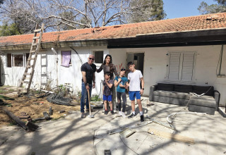 בני וימית אביטל עם ילדיהם על רקע ביתם ההרוס בניר עוז (צילום: פרטי)