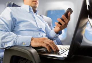 אדם משתמש בטלפון ומחשב נייד במטוס. אילוסטרציה (צילום:  אינגאימג')