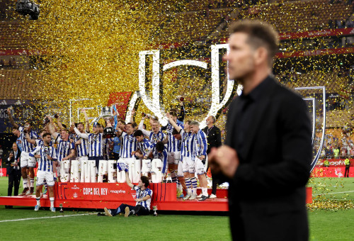 מאמן אתלטיקו מדריד דייגו סימאונה על רקע שחקני ריאל סוסיאדד מניפים את הגביע (צילום: אימג'בנק  GettyImages)