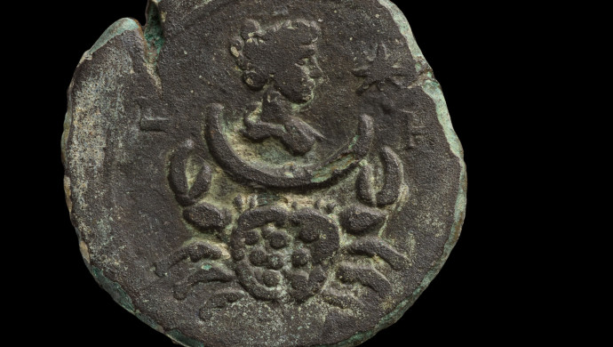 המטבע הנושא את דמותה של לונה, אלת הירח. מתחתיה מופיע סימן מזל סרטן. (צילום: דפנה גזית, רשות העתיקות)