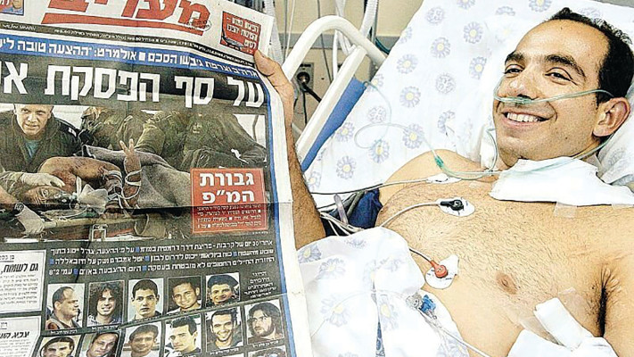 תומר בוהדנה בבית החולים לאחר הפציעה, עם התמונה האיקונית שלו