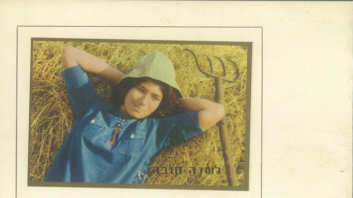 בחולצה כחולה עם כובע טמבל על ערימת חציר בשנות ה-50