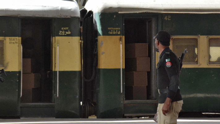 איש ביטחון פקיסטני ליד רכבת מלאה בארונות קבורה, בדרך לבולן - שם הותקפו הנוסעים (צילום:  REUTERS/Stringer)