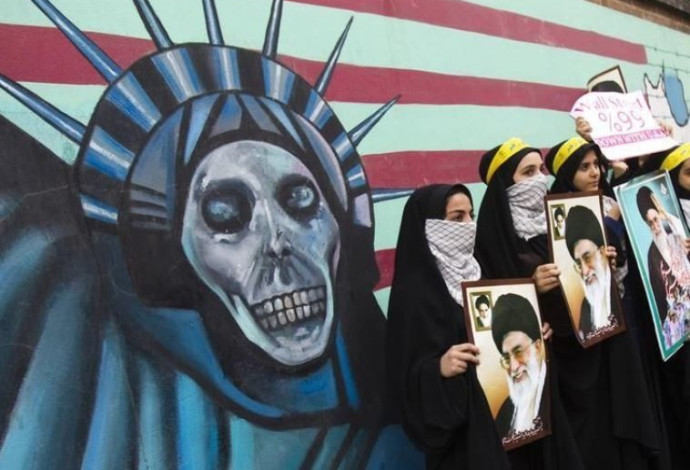 מפגינות איראניות מחזיקות בתמונתו של חמינאי לפני ציור אנטי אמריקאי (צילום:  רויטרס)