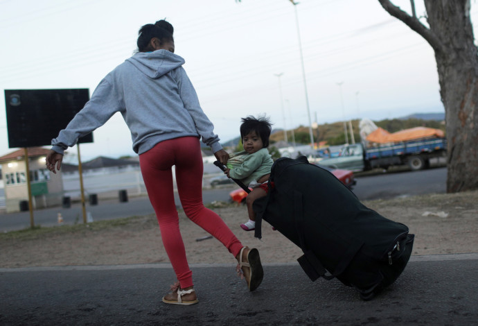 אישה המבקשת לחצות את הגבול מוונצואלה לברזיל לוקחת עמה את בנה על מזוודה (צילום:  רויטרס)