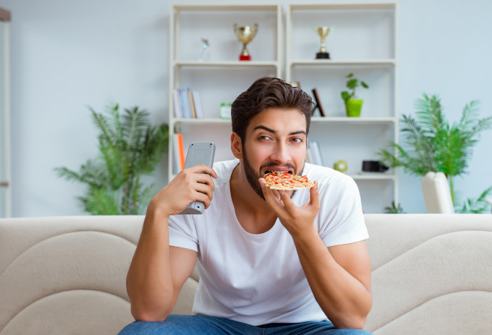 גבר אוכל פיצה בבית מול הטלוויזיה (צילום:  ingimage ASAP)