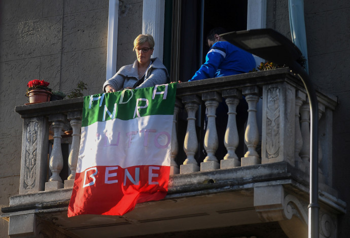 קורונה באיטליה: אישה מניחה את דגל איטליה עם הכיתוב: "הכל יהיה בסדר" על מרפסת ביתה (צילום:  רויטרס)