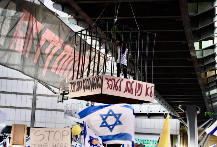 עינב צנגאוקר תלויה בכלוב מעל צומת בגין ביום השיבוש 7.7.24 (צילום:  אבשלום ששוני)