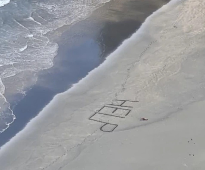 הזעקה לעזרה שכתב הגולש בחול (צילום: Surf Life Saving NZ)