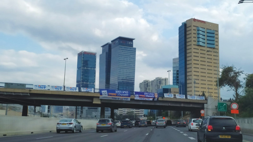 שלטים לא חוקיים תלויים על גשר מעל נתיבי איילון