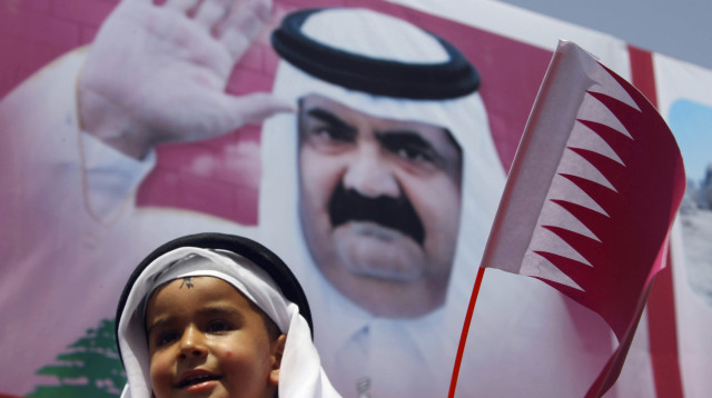 ילד מחזיק דגל קטאר על רקע תמונת האמיר (צילום: רויטרס)