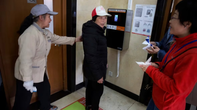 אישה מקרבת את הפרצוף שלה לזיהוי הפנים על מנת לקבל נייר טואלט (צילום: Ng Han Guan/Associated Press)