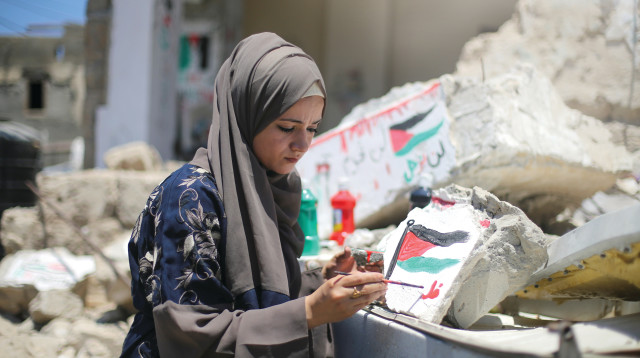 תושבת עזה מציירת דגל פלסטין על ביתה שנהרס במבצע "שומר חומות" (צילום: רויטרס)