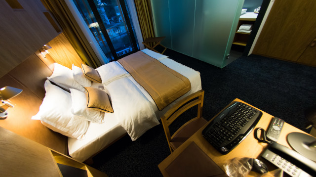 אורח נכנס לחדר המלון ונכנס לנוח על המיטה (צילום: אינג'אימג')