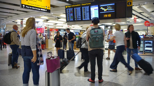 נוסעים מול לוח הטיסות בשדה התעופה בלונדון (צילום: שאטרסטוק)