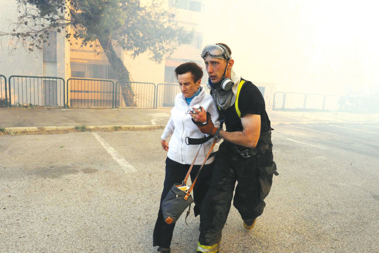לוחם אש מוביל קשישה למקום מבטחים מבין הבניינים המפויחים בחיפה. צילום: רויטרס