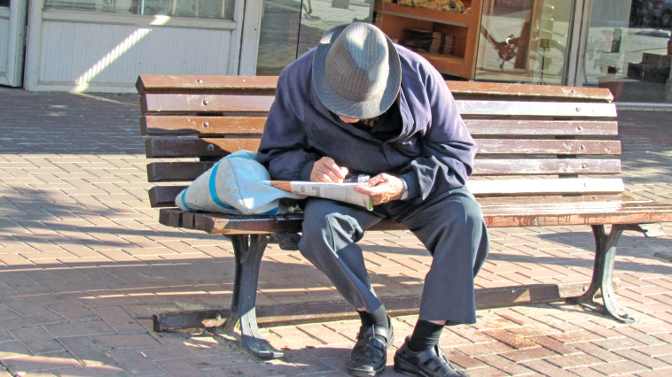 על ספסל ברחוב ויצמן יושב קשיש ופותר תשבץ. צילום: נתן זהבי