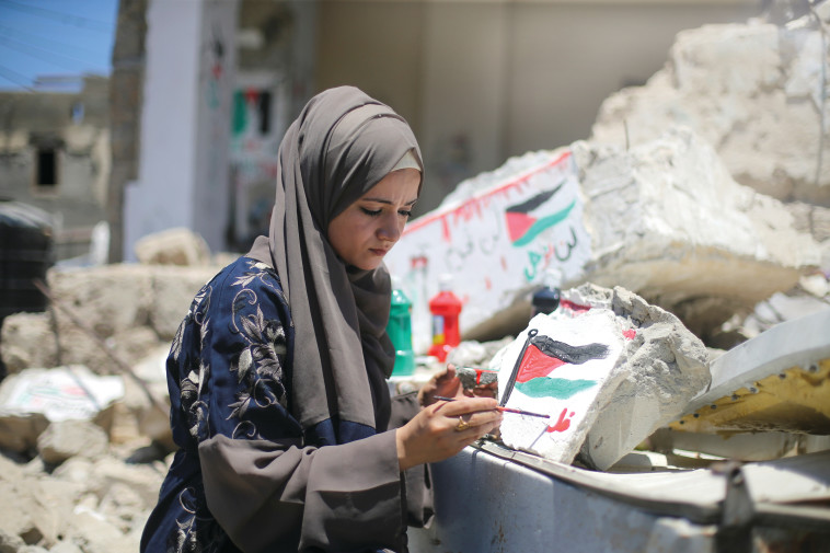 תושבת עזה מציירת דגל פלסטין על ביתה שנהרס במבצע ''שומר חומות'' (צילום: רויטרס)