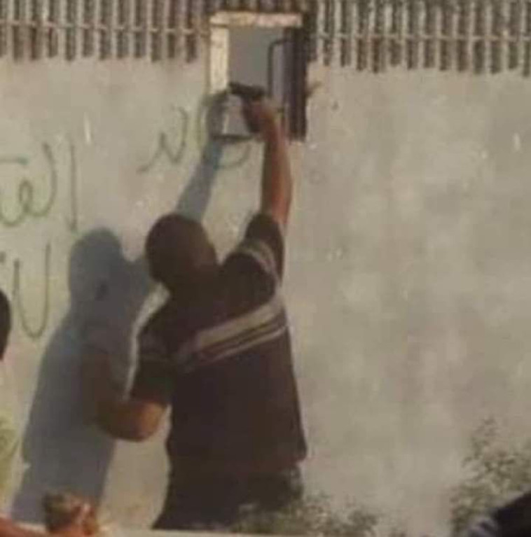 מפגין פלסטיני מכוון אקדח דרך גדר רצועת עזה