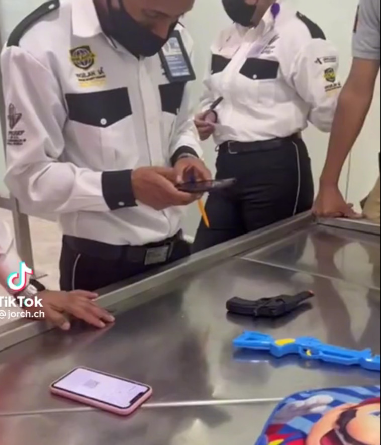 אקדחי הצעצוע מונחים על משטח הבידוק והמאבטחים מצלמים