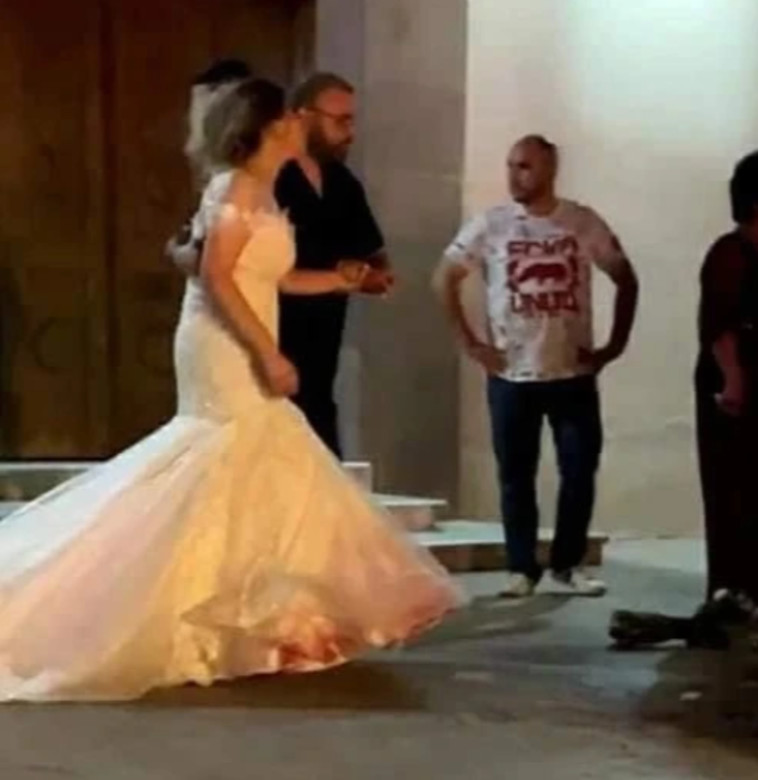 הכלה, אבודה ומלווה בבן משפחה כששמלתה מלוכלכת מדם אהובה