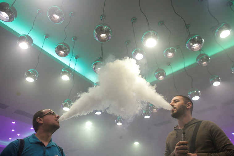 מעשנים נושפים את תוצר הסיגריות האלקטרוניות שלהם במהלך אירוע אידוי בבוקרשט, רומניה